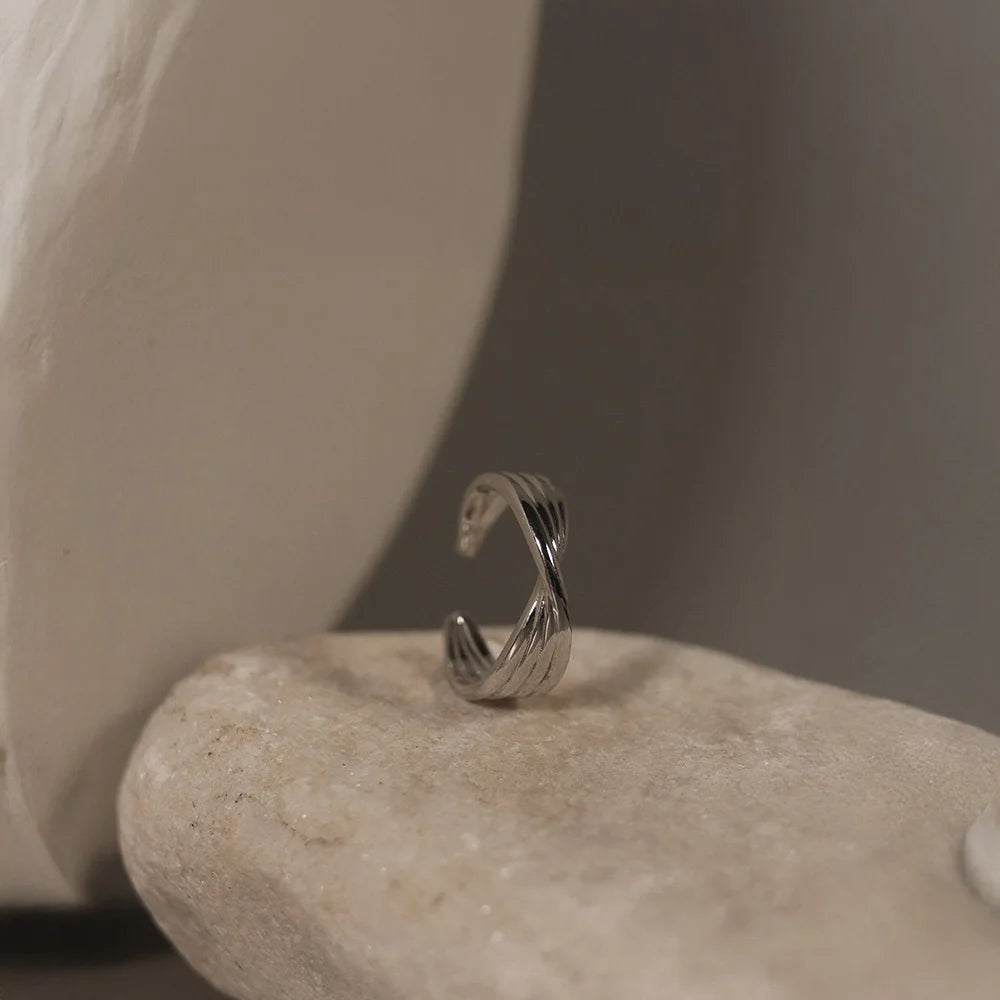 The silver twisted band mini ear cuff displayed on a natural white stone, showing its layered texture and polished finish.