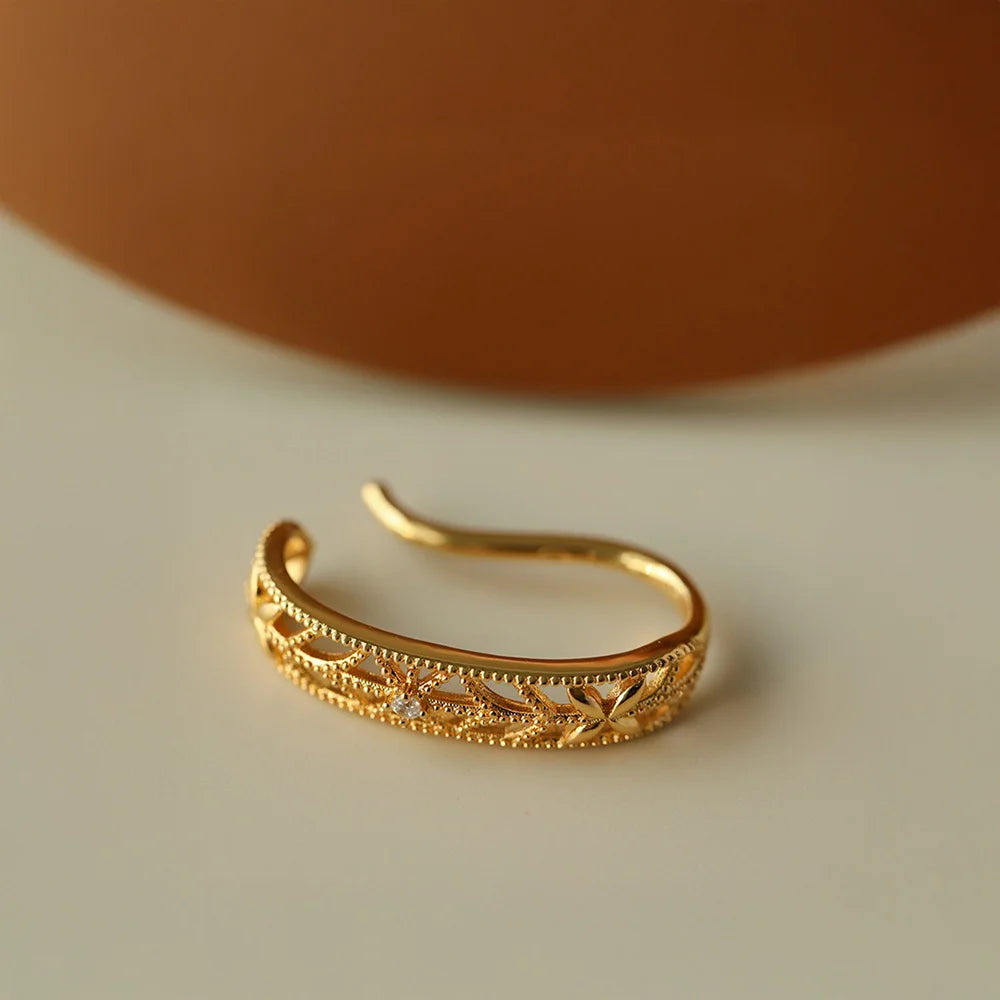 Detailed side view of the floral filigree gold ear cuff, highlighting the intricate cutout pattern and milgrain edges.