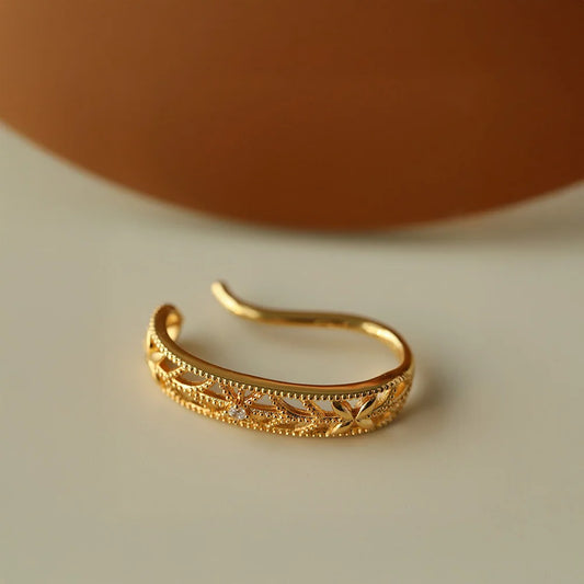 Detailed side view of the floral filigree gold ear cuff, highlighting the intricate cutout pattern and milgrain edges.