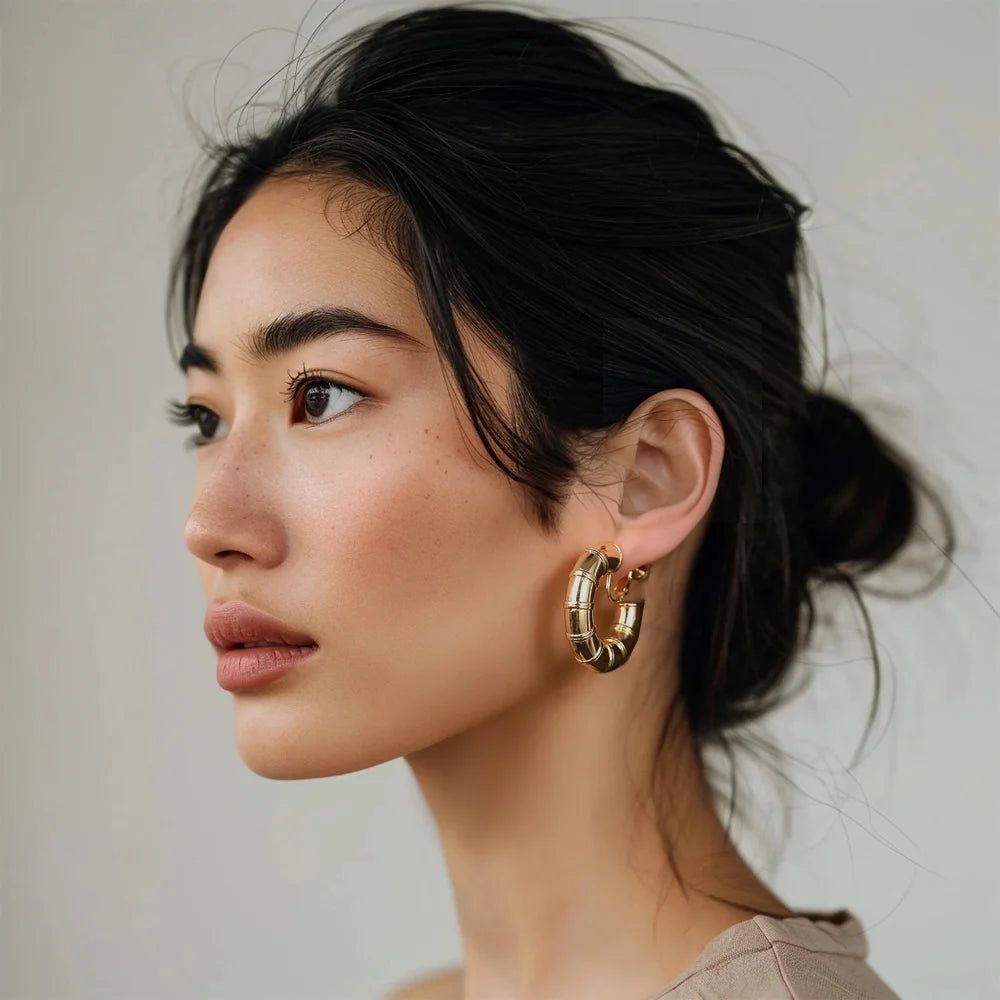 Woman wearing a pair of gold bamboo hoop clip-on screw back earrings on a white background