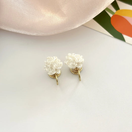 A pair of white resin flower clip-on earrings with comfortable mosquito coil clips displayed on a white surface next to a satin cloth.