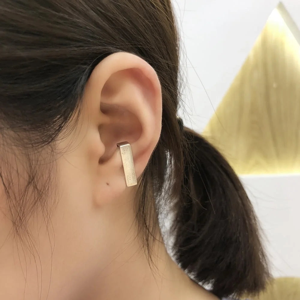 A close-up of a woman's ear wearing a single, modern rectangular bar ear cuff made of sterling silver on her conch for a minimalist look.