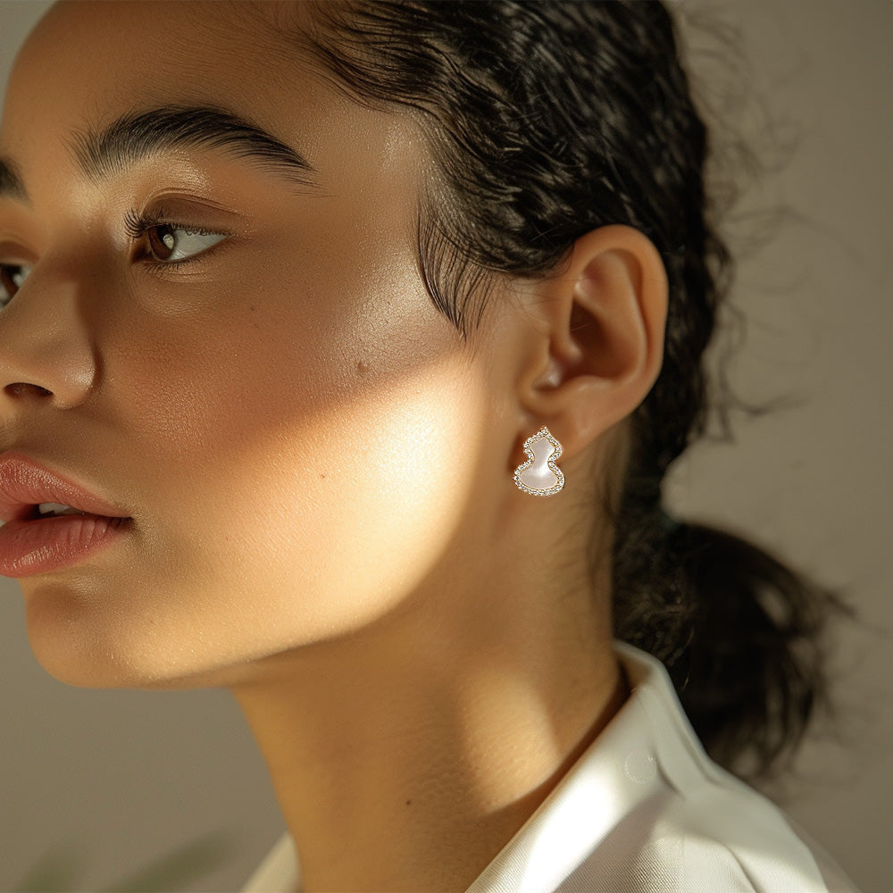 Model wearing Wulu petite clip-on earrings in gold and white. These earrings feature a delicate mother-of-pearl gourd accented with cubic zircons. Crafted from gold-tone alloy with a coil clip closure for pierced ears. Embrace a touch of ancient Chinese tradition in a charming and modern design.