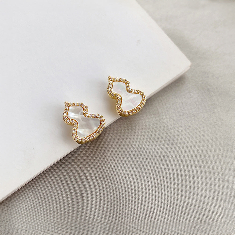 Wulu petite clip-on earrings in gold and white. Luminous mother-of-pearl gourd with sparkling zircons. Gold-tone alloy with coil closure. Attract positive vibes and elevate your festival fashion with a touch of cultural flair. 