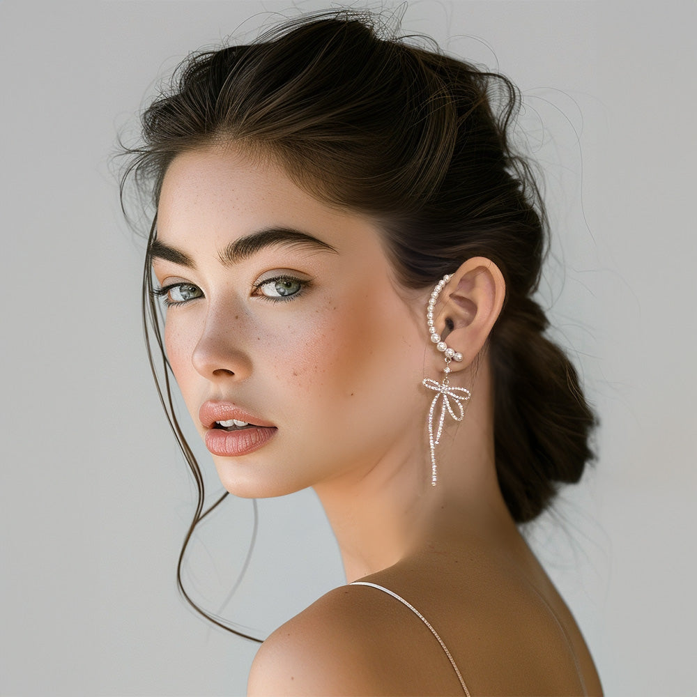 Silver tone ear wrap cuff earring adorned with a delicate bow design and cascading faux pearls. This cuff earring adds a graceful touch to any wedding attire and is perfect for formal occasions, providing a classic yet distinctive look.