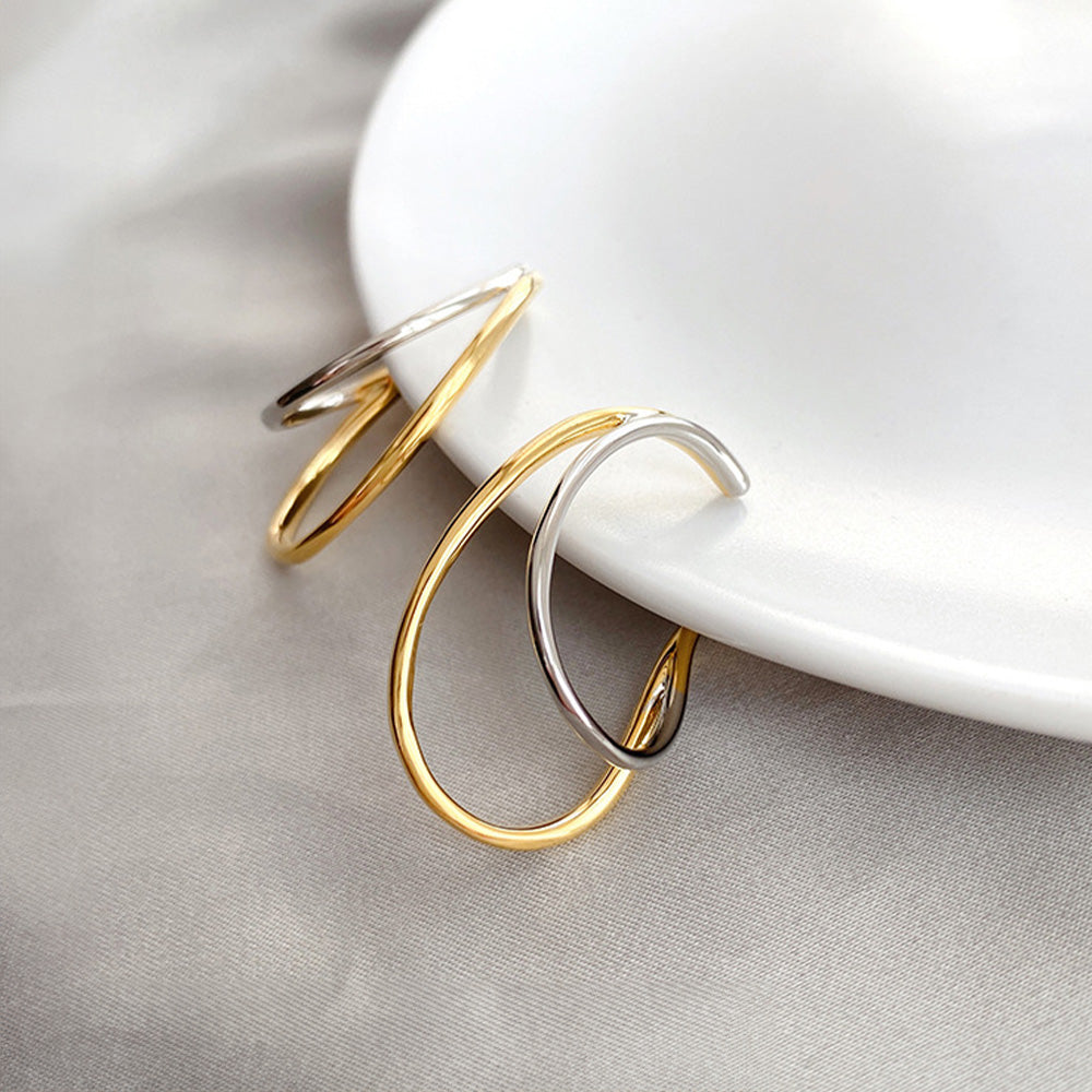 A pair of Dual-Tone Wave Conch Ear Cuffs resting on a white ceramic plate, highlighting the contemporary wave design in gold and silver tones that complement both everyday and workwear without the need for piercings.