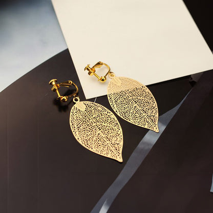 Elegant screw-back clip-on earrings featuring delicate gold-tone leaves, reflecting a modern take on nature-inspired jewelry crafted from a copper alloy.