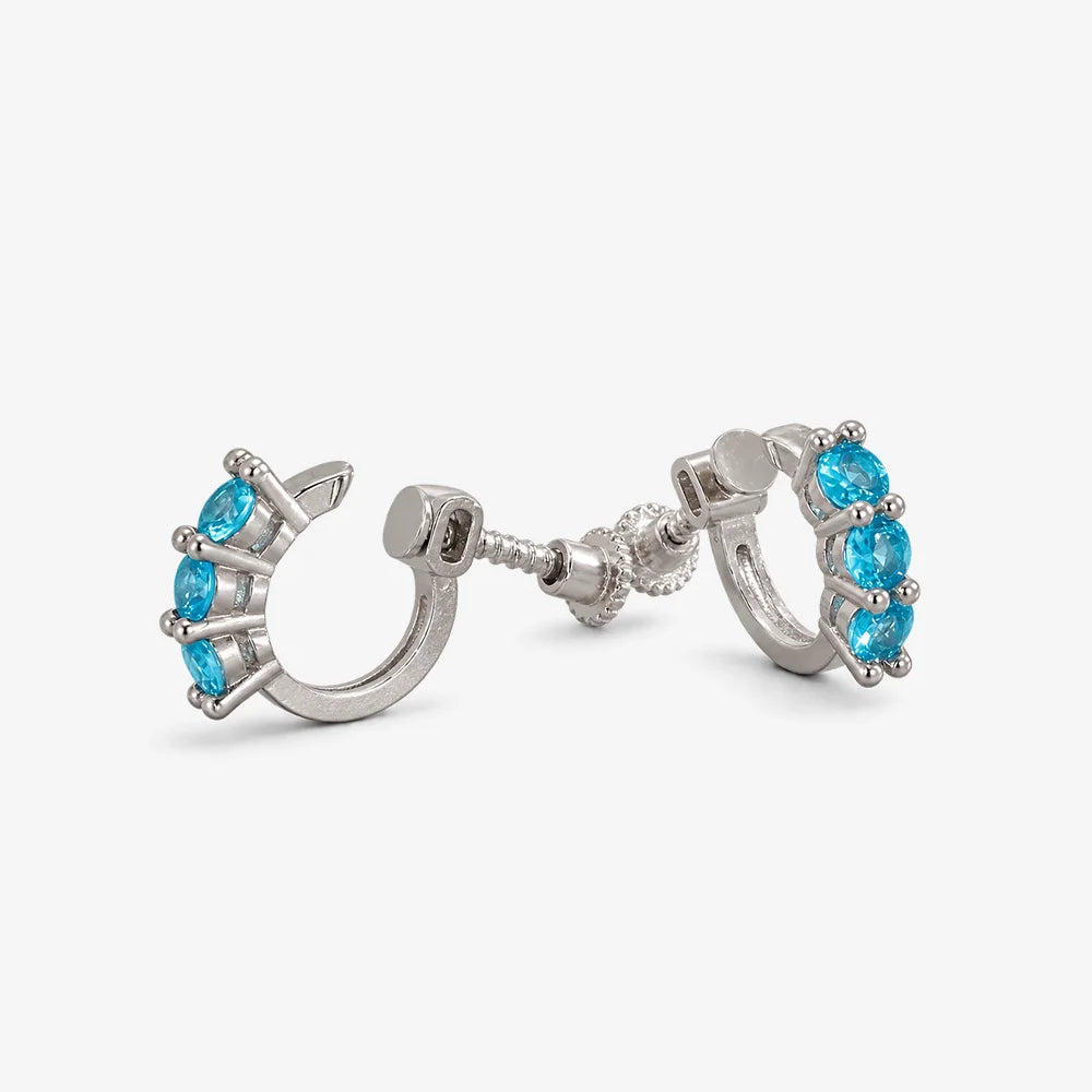 A pair of silver huggie hoop earrings with small oval blue gemstones, shown on a light gray background.