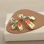 Asymmetric Color-Brush Petal Clip-On Earrings in gold with blue and red painted details, displayed on tan and white presentation stand