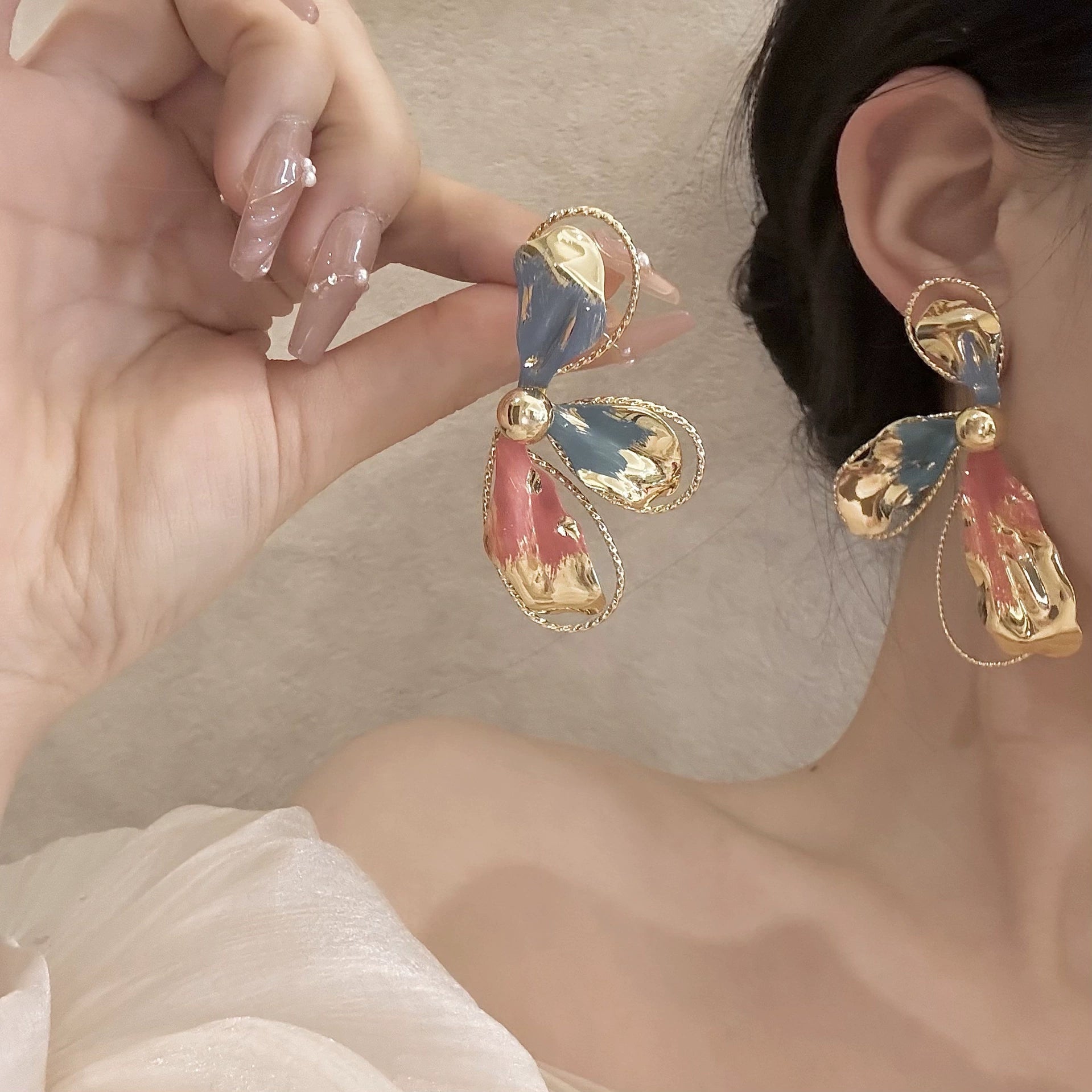 Asymmetric color-brush petal clip-on earrings in gold with blue and red enamel worn on model, side view