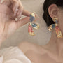 Asymmetric color-brush petal clip-on earrings in gold with blue and red enamel worn on model, side view