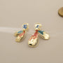 Asymmetric color-brush petal clip-on earrings in gold with blue and red enamel details, front view on beige background