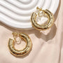 Gold bamboo hoop clip on earrings displayed on white ceramic dish and beige surface, top view