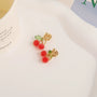 Beaded cherry clip-on earrings with green leaves and gold details on white background, top view