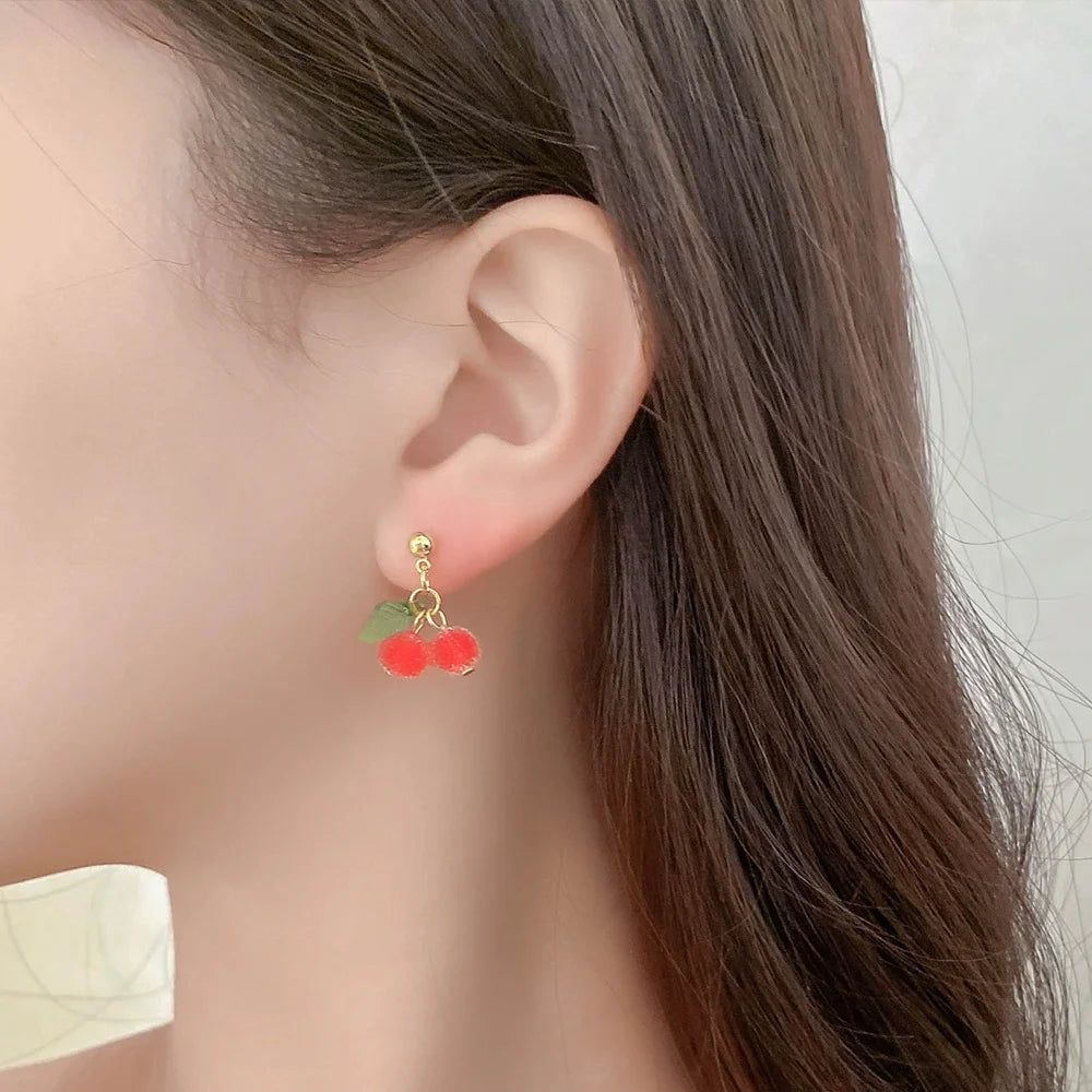 Beaded cherry clip-on earrings with green leaves, side view on model with long brown hair