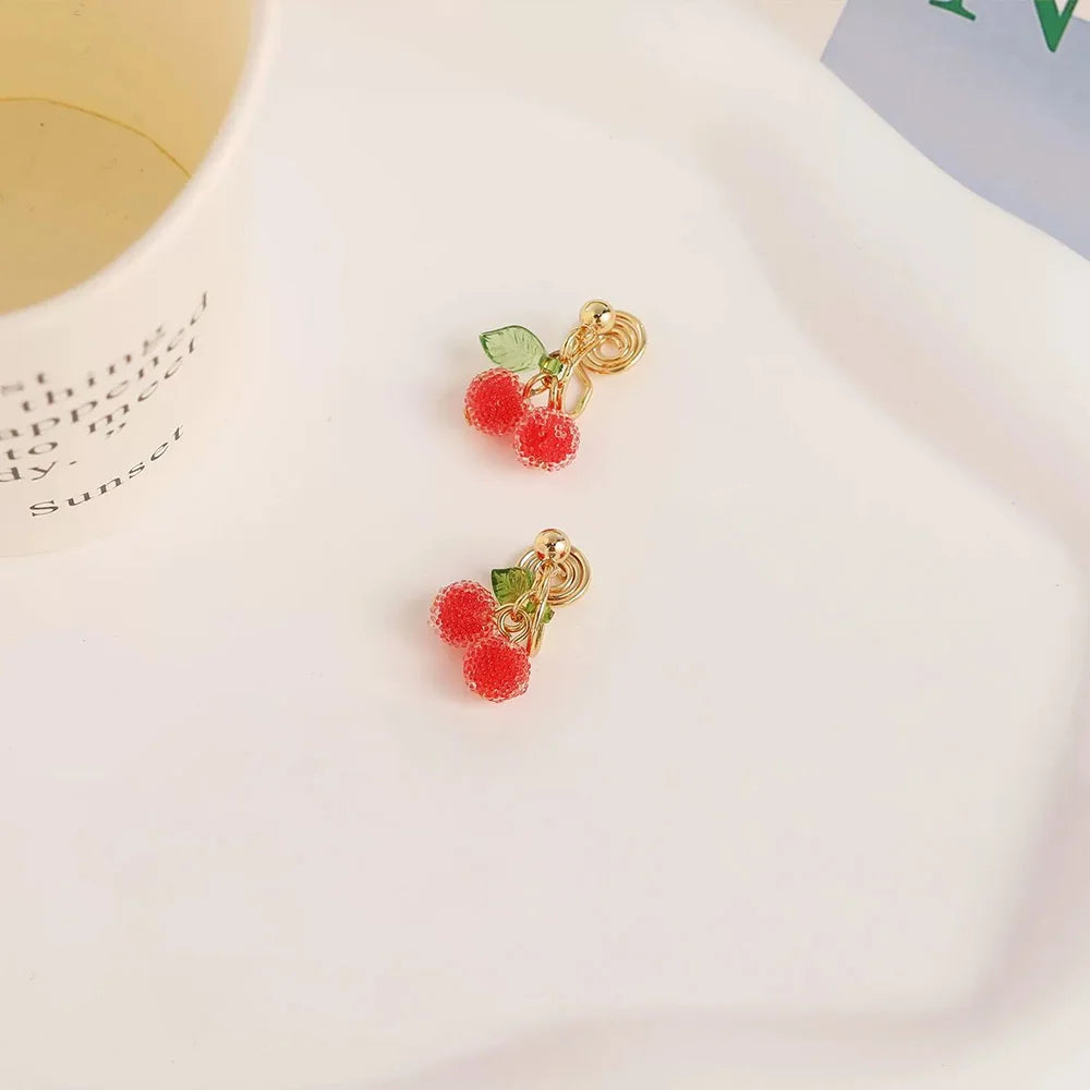 Beaded cherry clip-on earrings with green leaves, gold-toned hardware, displayed flat lay on white background