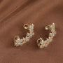 Gold Blossom Flower Ear Cuff pair displayed on tan fabric background, showcasing intricate crystal details and hook closure design