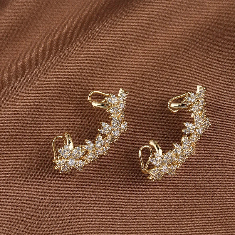 Gold Blossom Flower Ear Cuff pair displayed on tan fabric background, showcasing intricate crystal details and hook closure design