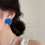 Blue Bloom Floral Clip-On Earrings worn on ear, side view with dark hair and pearl necklace