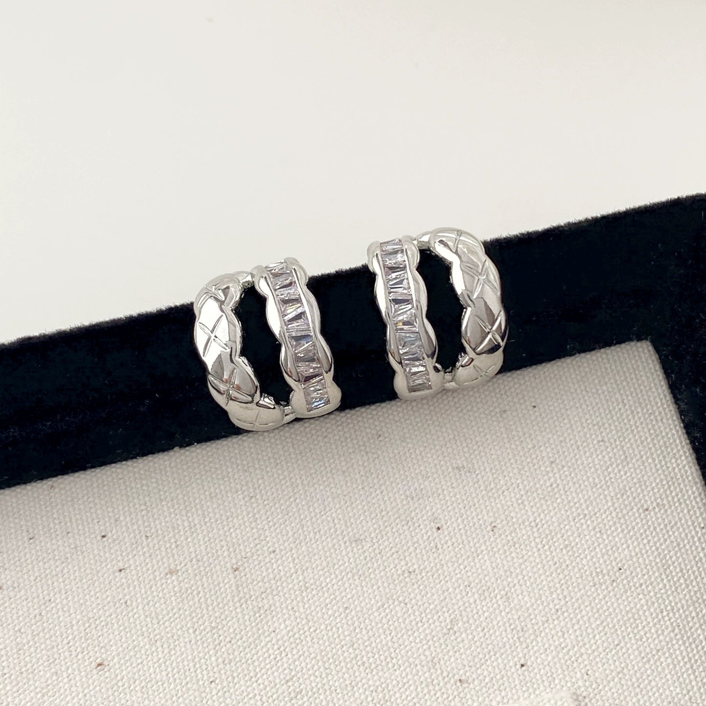 Pair of white gold hoop earrings on a black velvet stand with a white background.