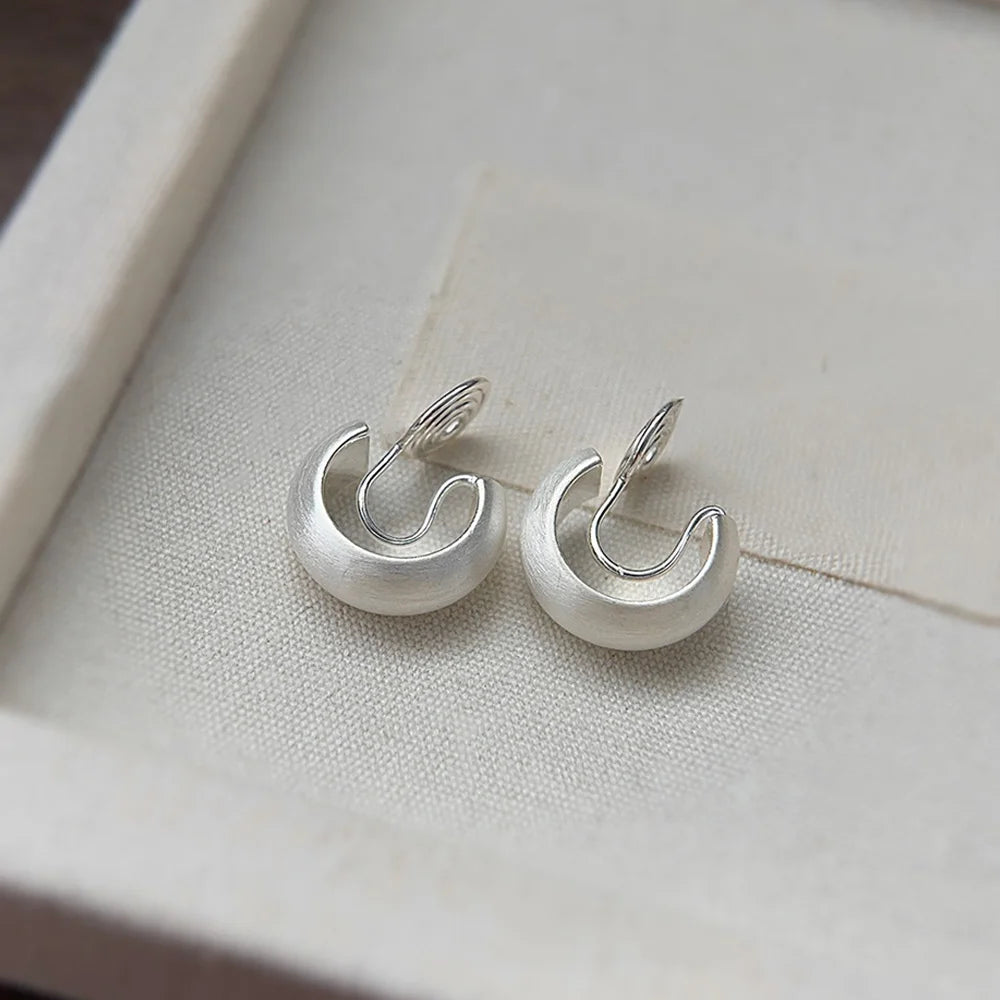 Boucles d'oreilles créoles à clip argentées, dotées d'une texture brossée moderne et d'un système de fixation en forme de U.
