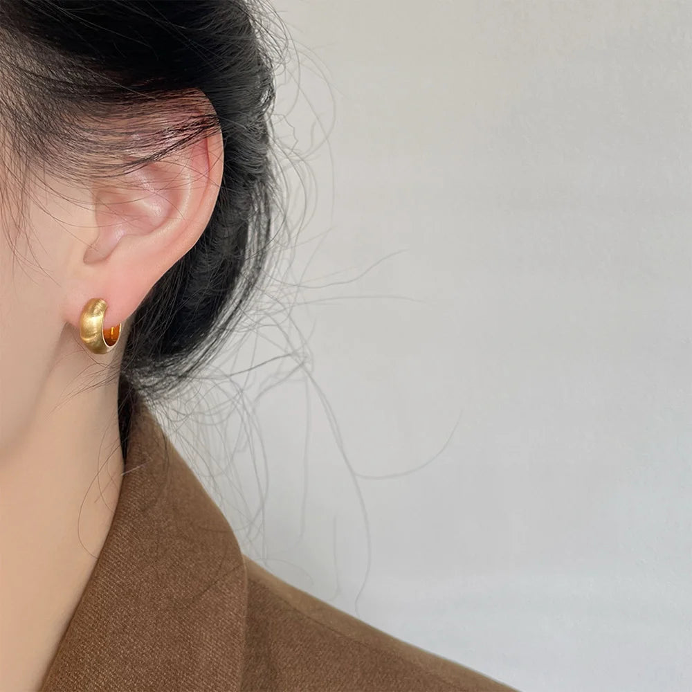 Brushed gold clip-on hoop earrings side view worn on ear against white background