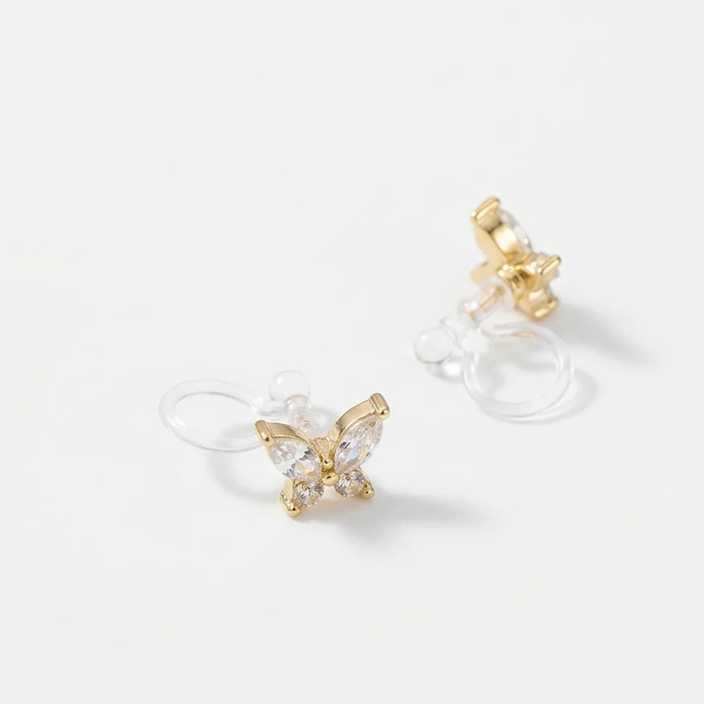 Gold butterfly stud earrings with clear crystal wings and clear silicone ear clip hooks, shown on a clean white background.