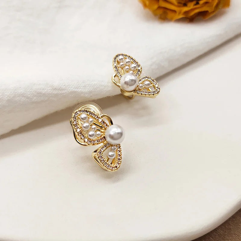 Gold butterfly wing clip-on pearl earrings displayed on white marble surface showing filigree detail and lustrous pearls
