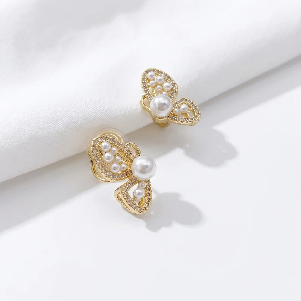 Gold butterfly wing clip-on pearl earrings displayed on white marble surface showing filigree detail and lustrous pearls