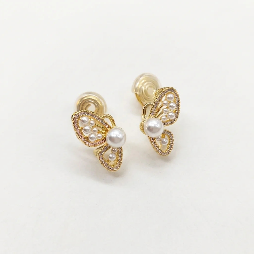 A pair of gold butterfly stud earrings decorated with white pearls and small clear rhinestones, set against a plain white background.