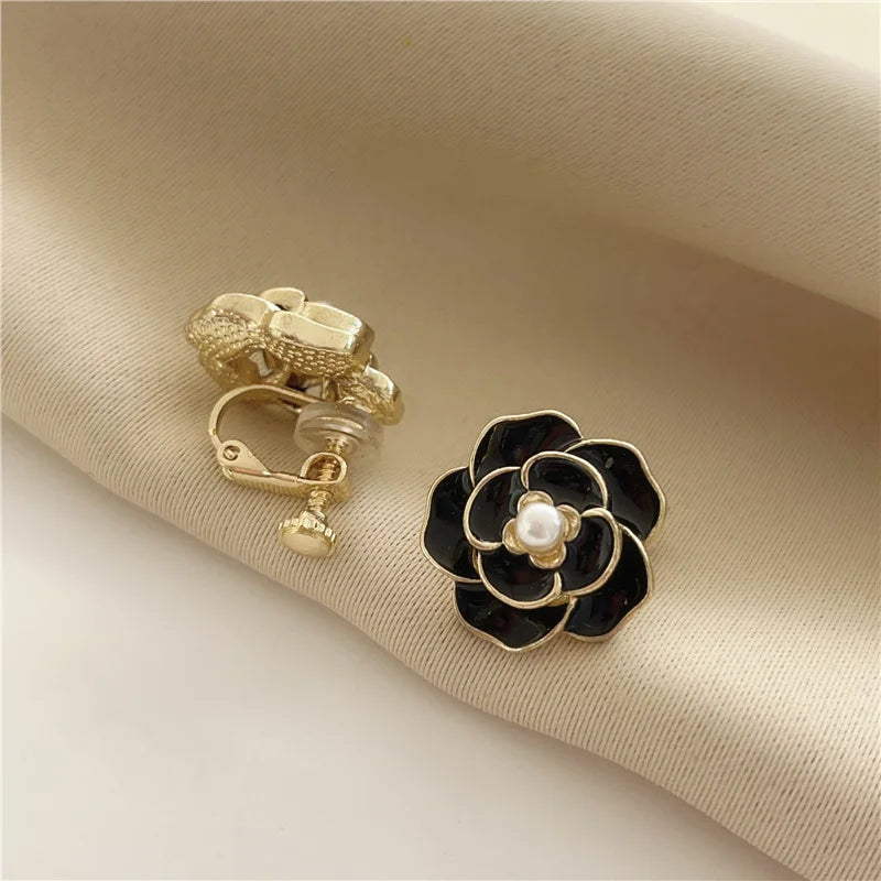 Black camellia enamel clip-on earrings with pearl center on beige fabric, gold-tone metal detail view