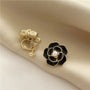 Black camellia enamel clip-on earrings with pearl center on beige fabric, gold-tone metal detail view