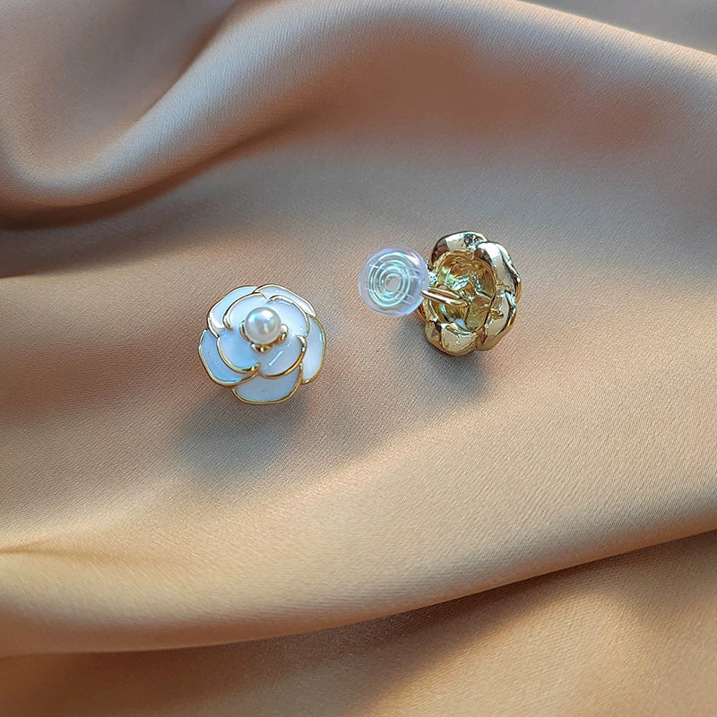 Paire de boucles d'oreilles en forme de fleur, dorées et blanches, sur fond de tissu beige.