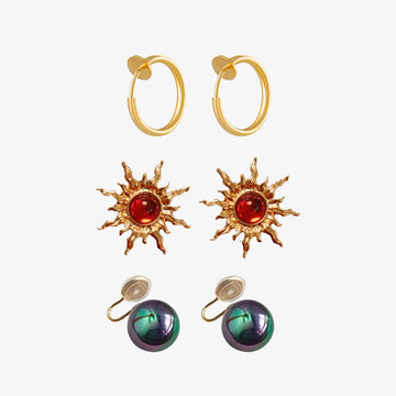 Celestial Glow Trio Clip-On Earring Set featuring gold hoops, sun motifs with red stones, and iridescent spheres on white background