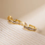 Gold channel-set zirconia clip-on hoop earrings displayed on white textured surface, angled side view