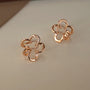 Élégantes boucles d'oreilles manchette en or rose, ornées de fleurs de cerisier, reposant sur un support traditionnel sombre, leur design en forme de sakura étant mis en valeur par un travail artisanal complexe et un accent central en zircon.