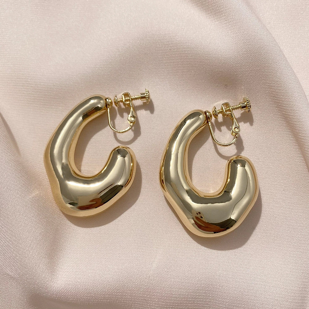 Chunky curved gold hoop clip-on earrings displayed on white fabric, showing polished metallic finish and elegant curved design from front angle