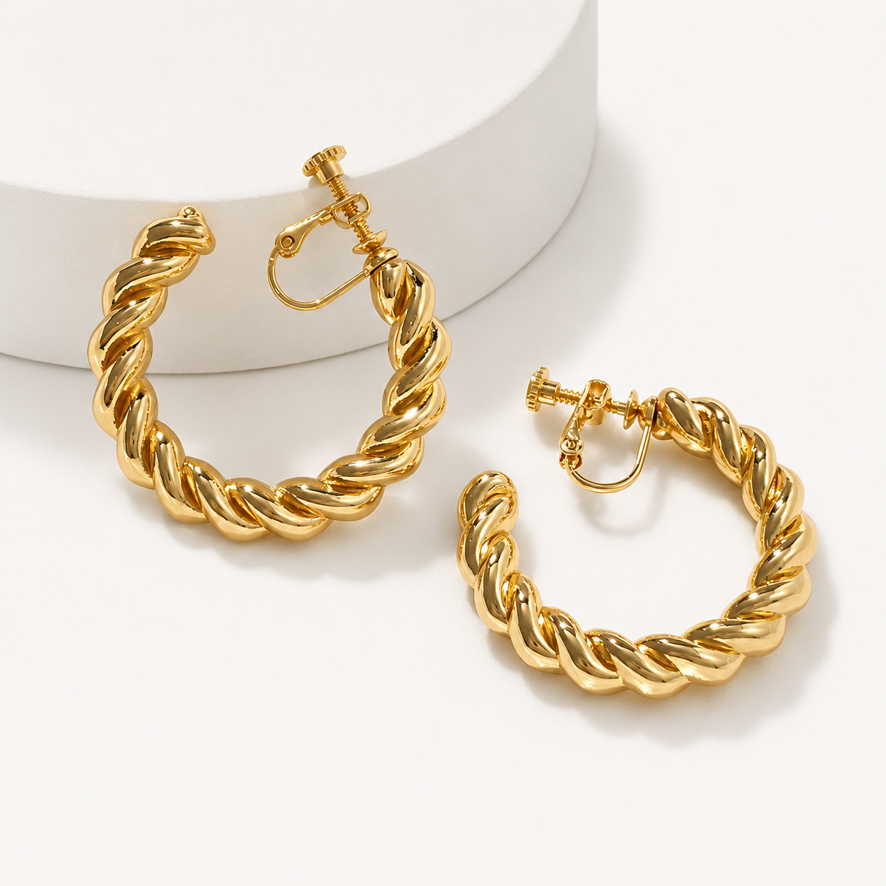 Gold twist hoop clip-on earrings displayed on white background showing detailed spiral design and secure closure mechanism
