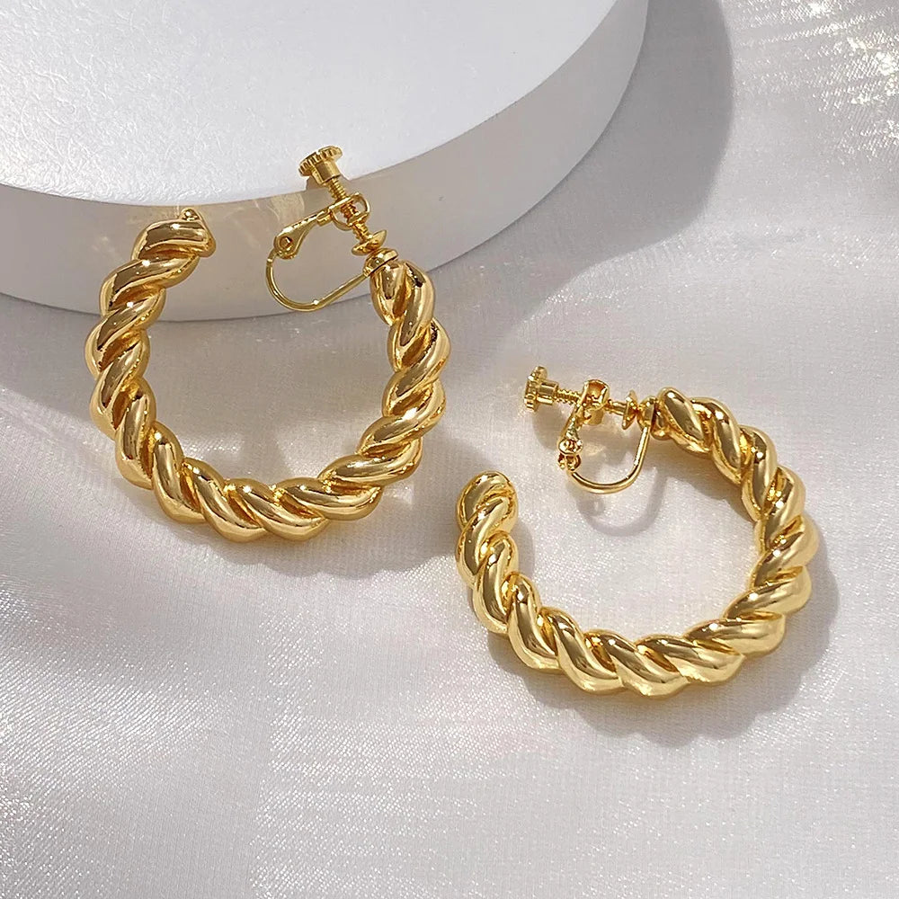 Gold twist hoop clip-on earrings displayed on white background showing detailed spiral design and secure closure mechanism