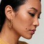 A close-up side profile of a woman wearing a textured gold hoop earring