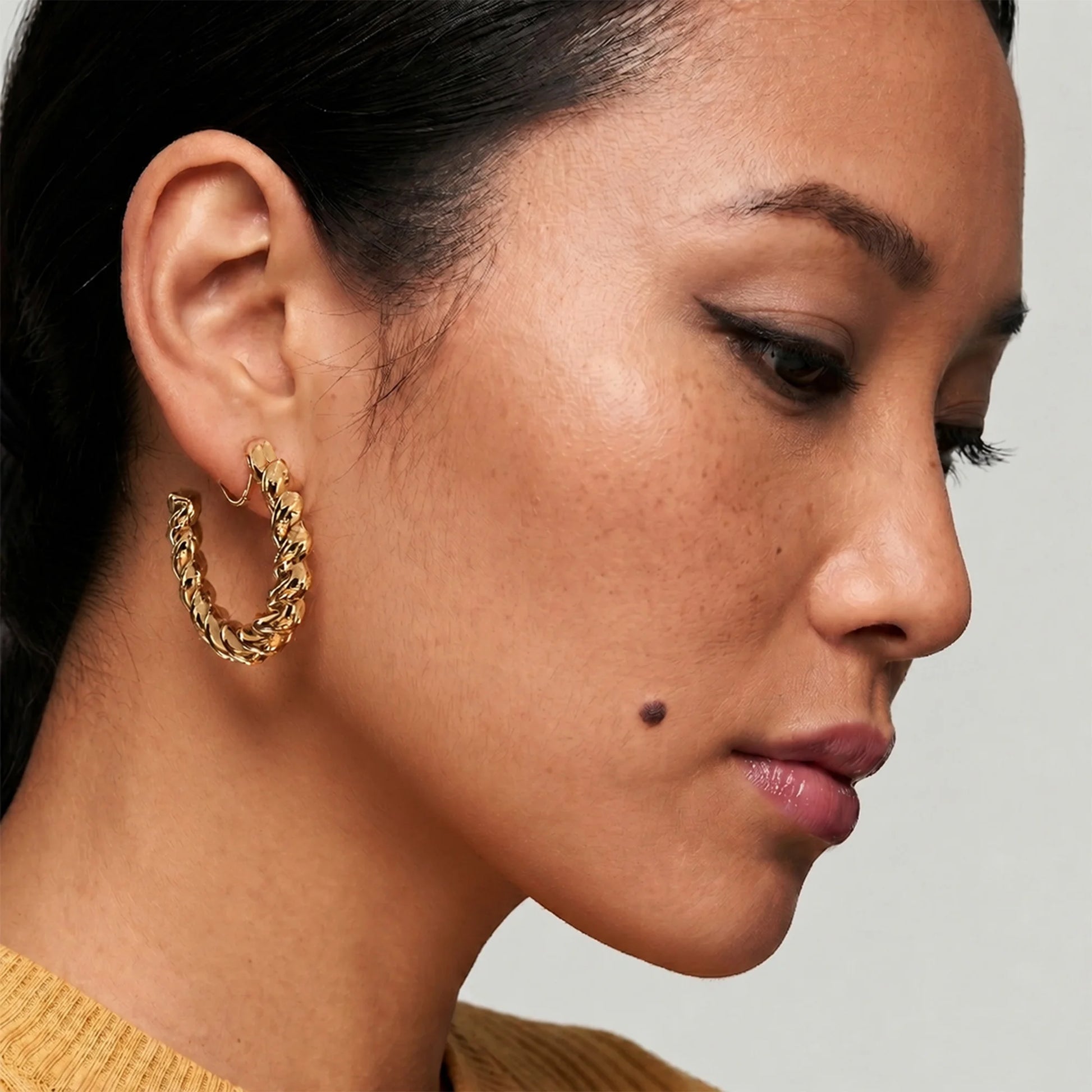 A close-up side profile of a woman wearing a textured gold hoop earring