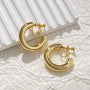 Gold classic hoop clip-on earrings displayed on white textured background with pleated detail