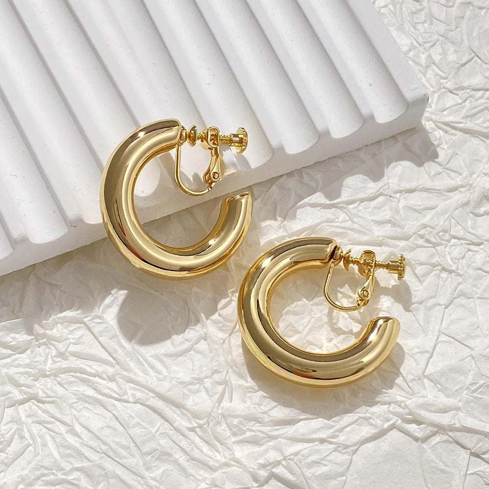 Gold classic hoop clip-on earrings displayed on white textured background with pleated detail