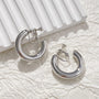 Silver classic hoop clip-on earrings displayed on white textured background showing polished metal finish and secure closure mechanism