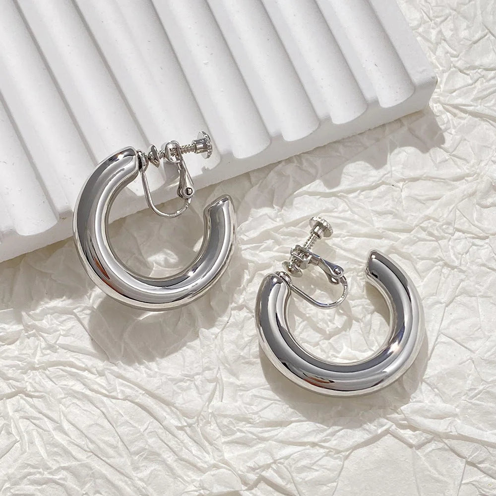 Silver classic hoop clip-on earrings displayed on white textured background showing polished metal finish and secure closure mechanism