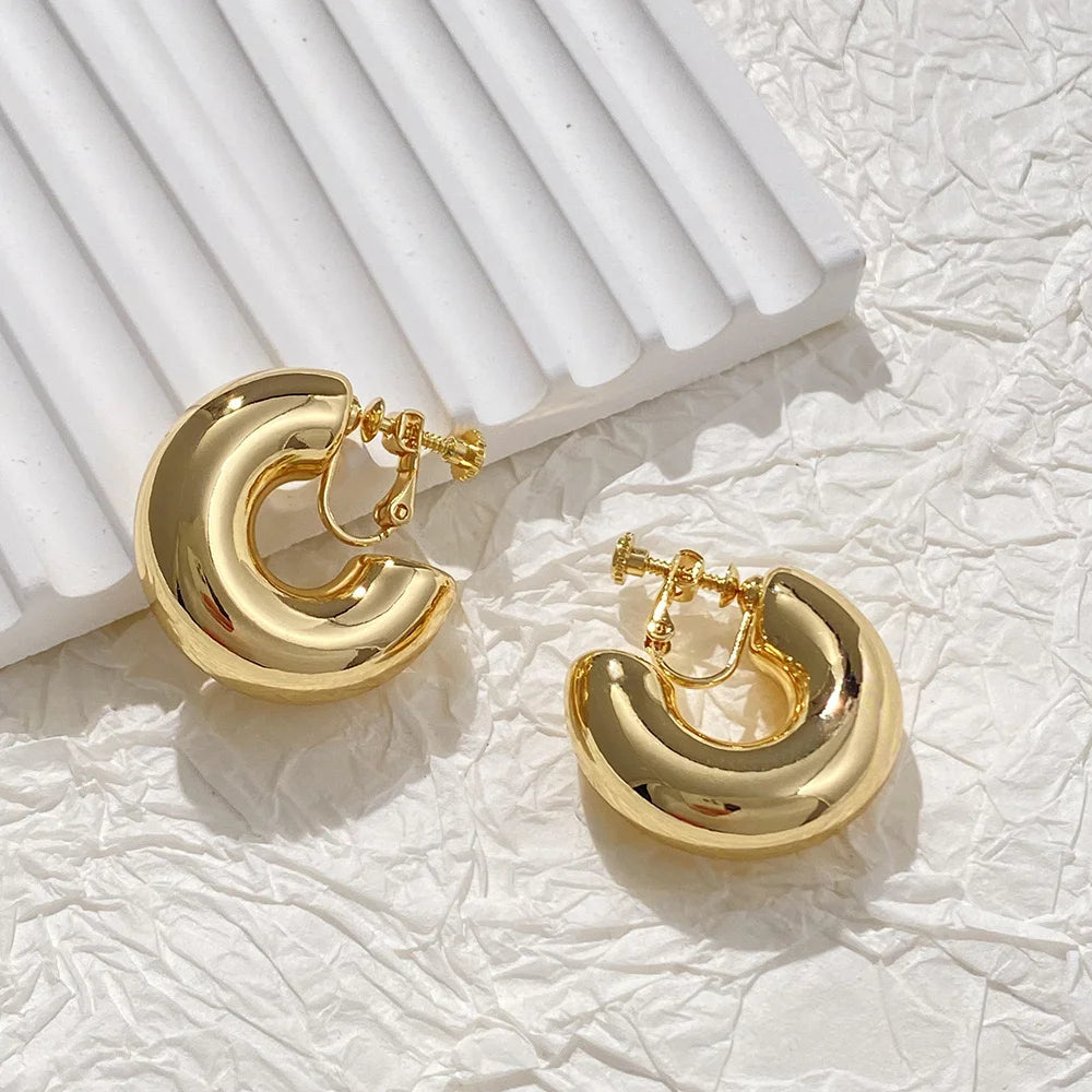 Gold classic bold hoop clip on earrings displayed on white textured background with shadows