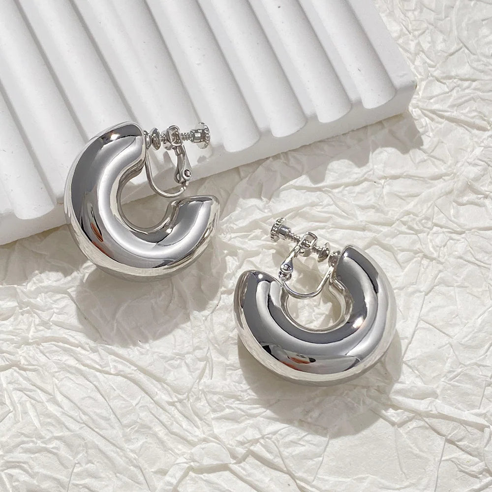 Classic bold silver hoop clip-on earrings displayed on white textured fabric background