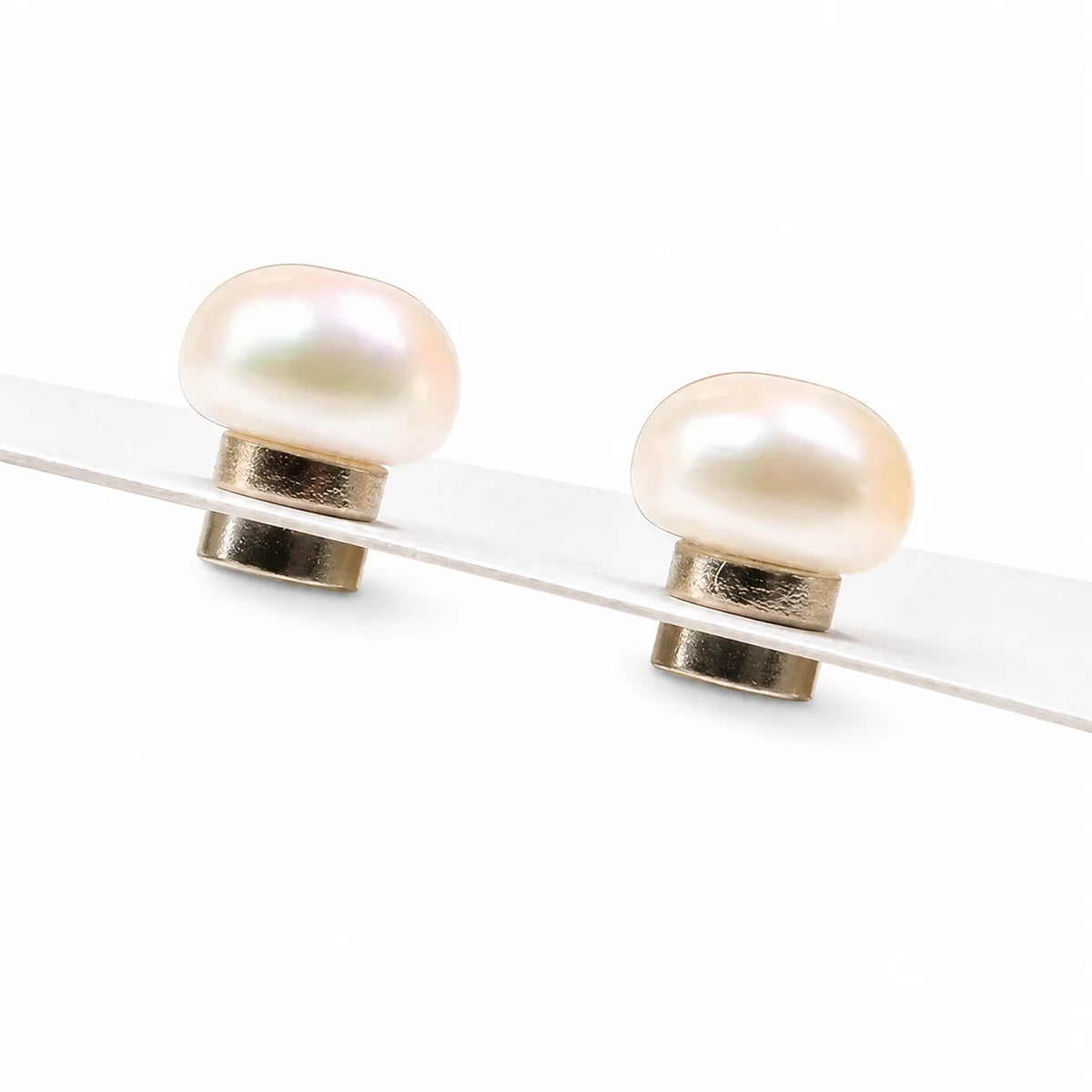 A pair of stud earrings featuring smooth, oval-shaped cream-colored pearls set in polished, displayed on a clean white background.