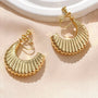 Gold croissant semi hoop clip-on earrings displayed on beige fabric with white ceramic dish, overhead angle view
