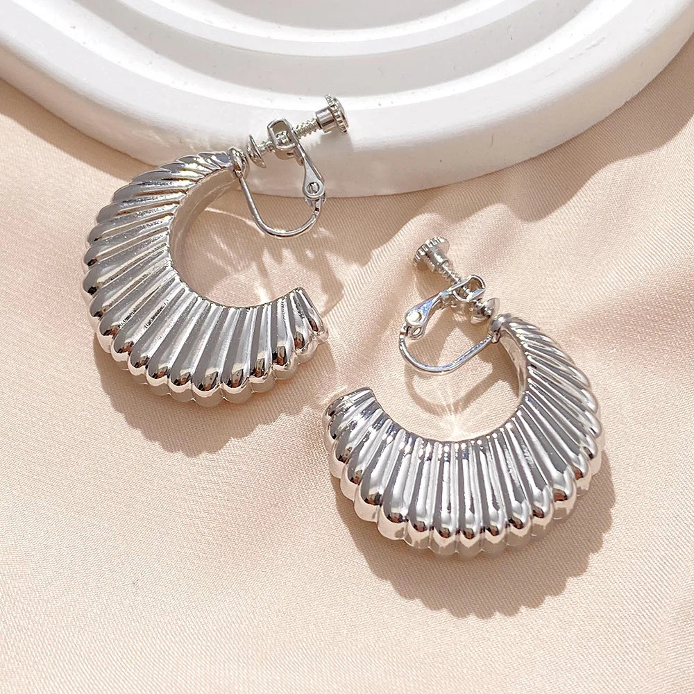 Silver croissant semi hoop clip-on earrings displayed on beige fabric, showing detailed ridged texture and shine from above